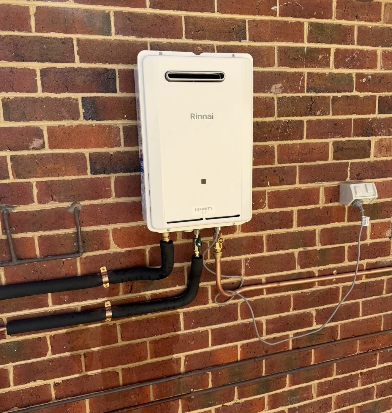 Rinnai Infinity continuous flow gas hot water unit installed on a brick wall in Perth with neat copper and insulated pipework